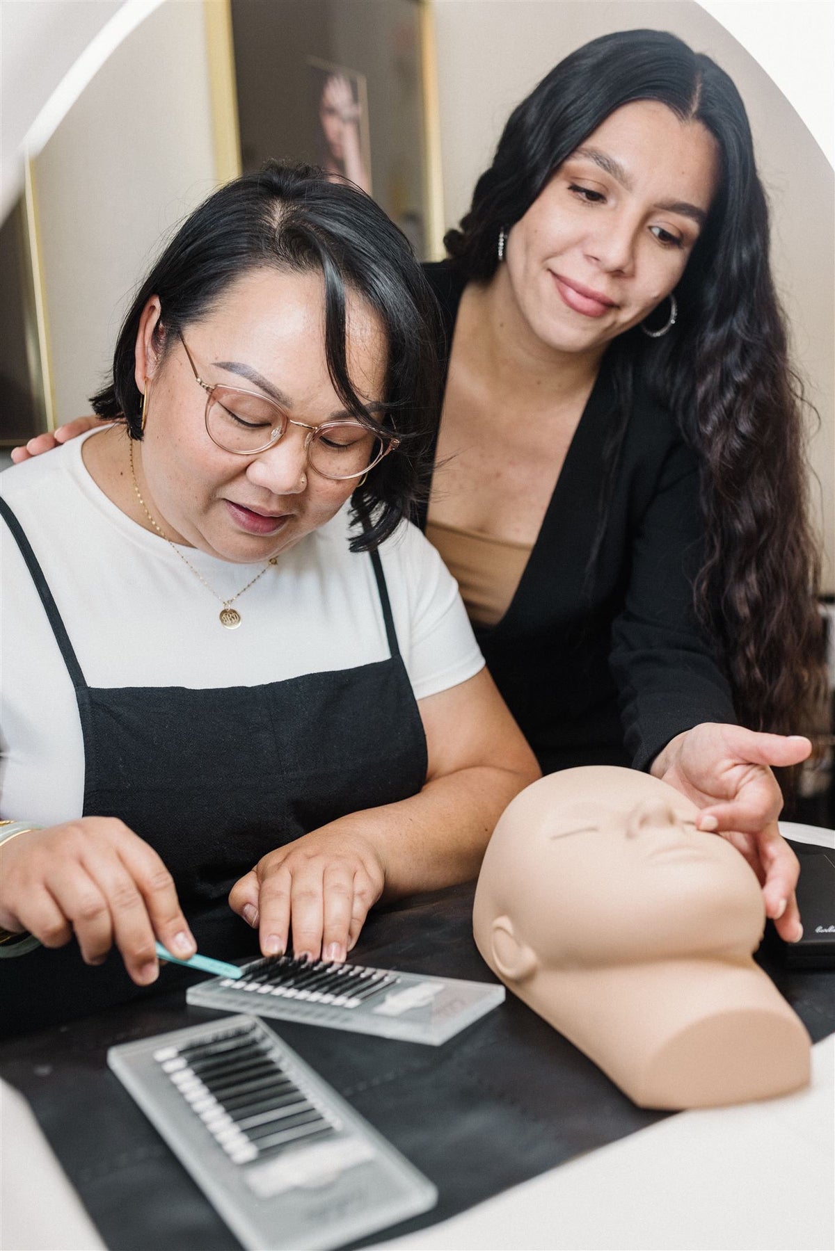 Hands practicing lash technique with lash trays and a training mannequin